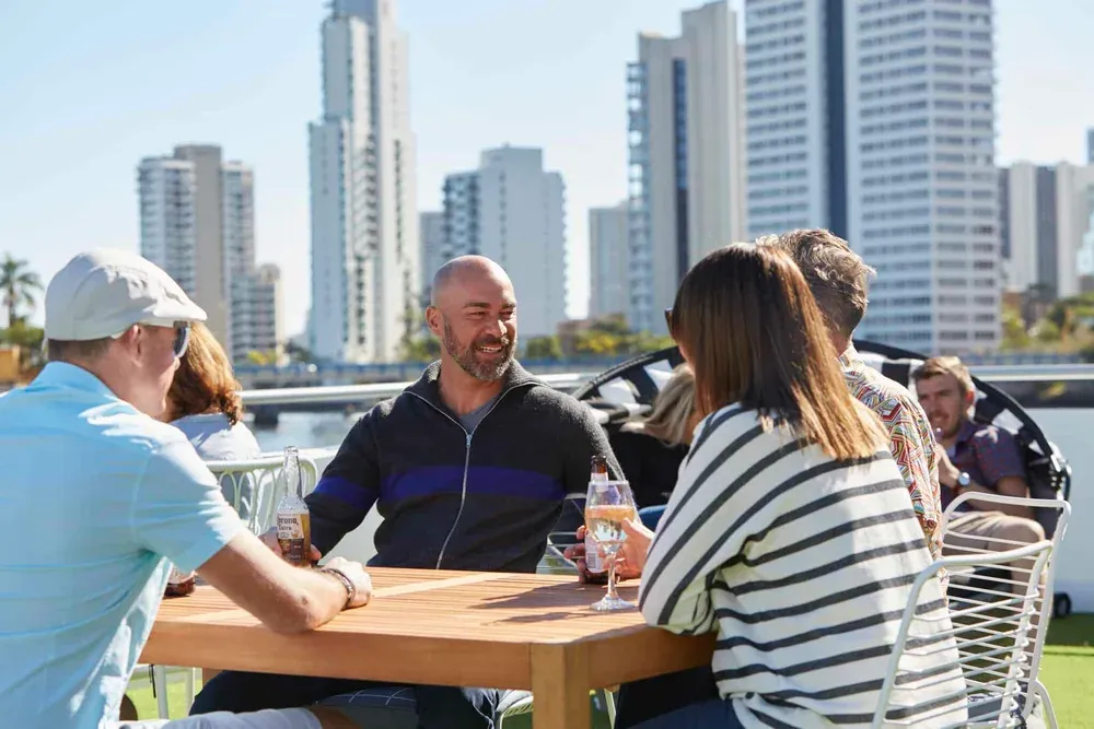 Guests talking around a table on the open deck beside the city skyline